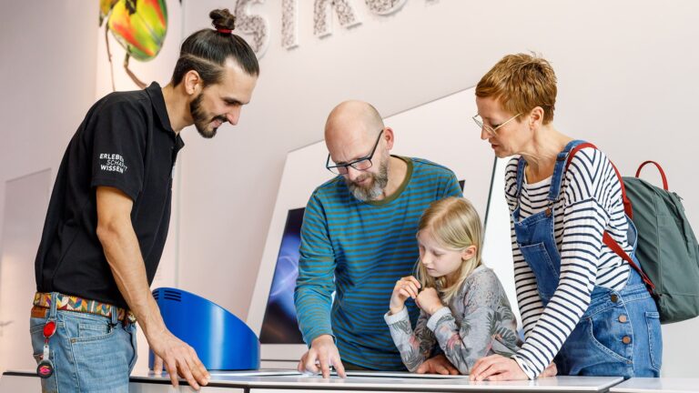 Eine Familie und ein Besucherbetreuer betrachten eine Station in der experimenta-Ausstellung