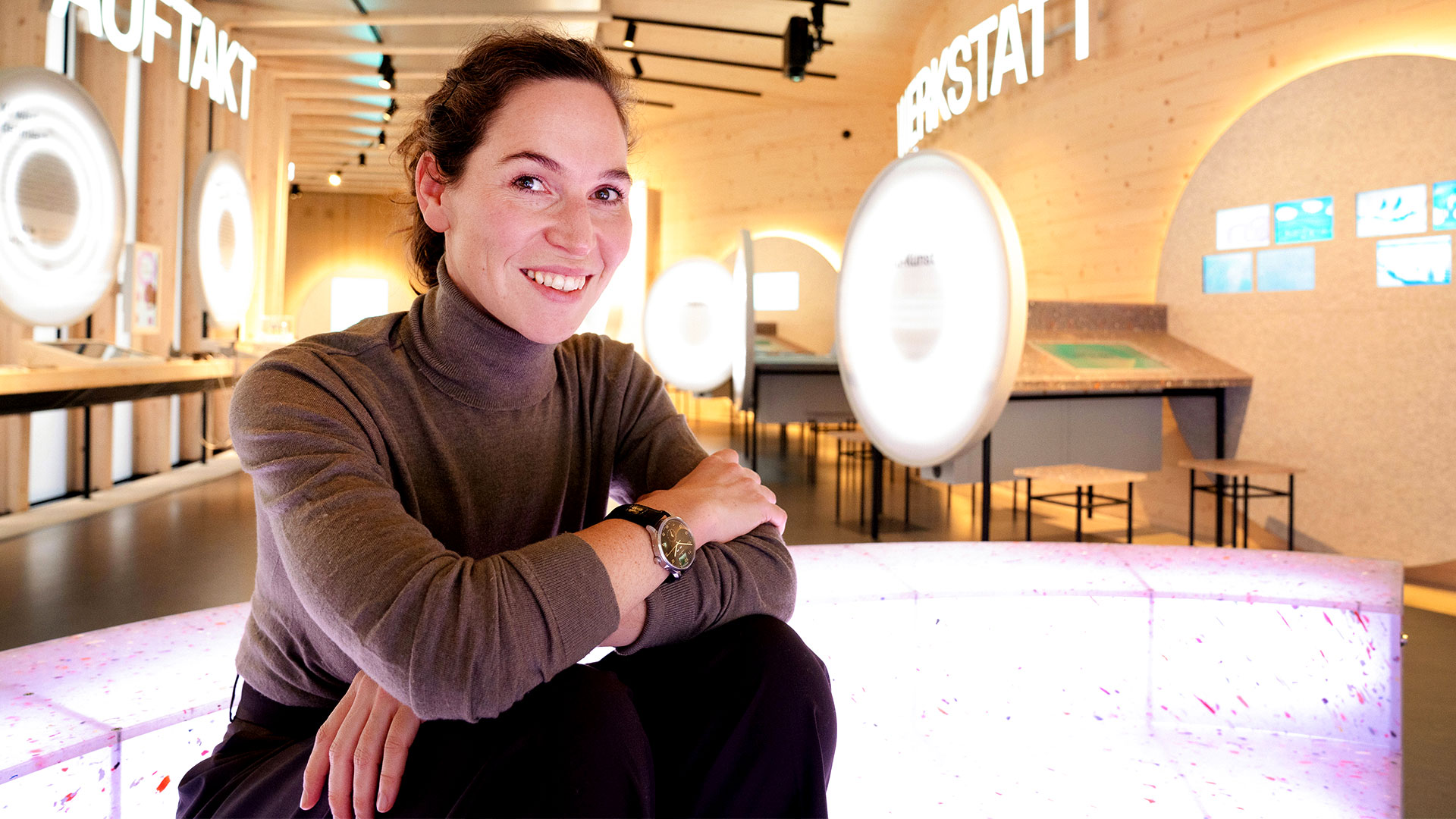 Cecilia Preiß im KI-Pavillon der experimenta Heilbronn, sitzend vor interaktiven Stationen der Ausstellung zu Künstlicher Intelligenz